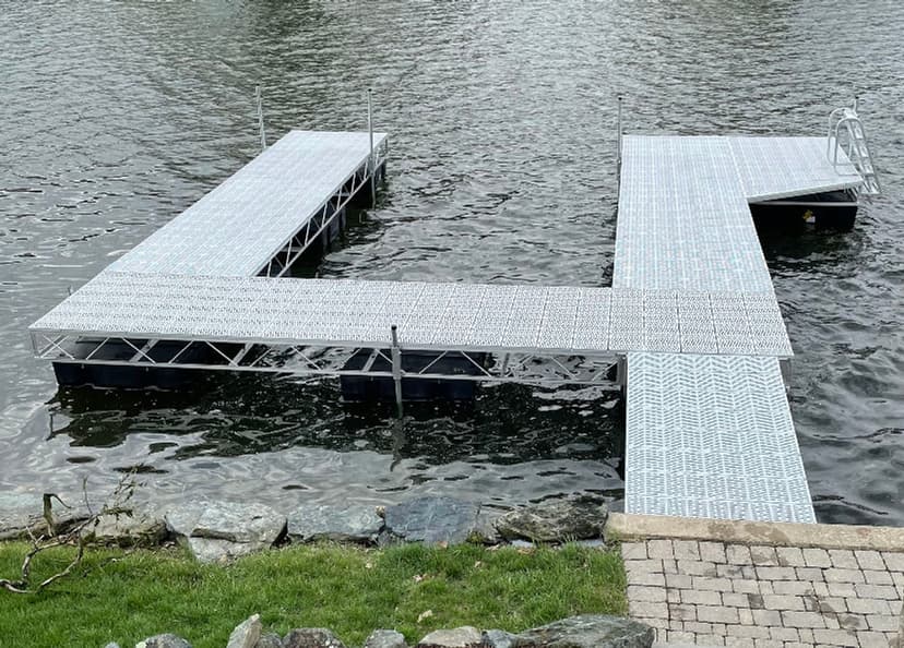 Aluminum boat dock on calm water with stone shoreline and green grass.