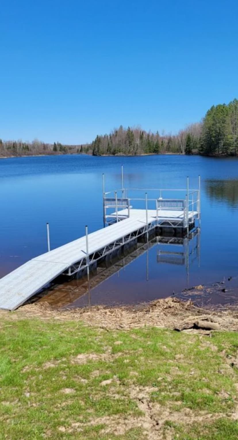 Dock on serene lake reflecting clear blue sky and green trees, ideal for relaxation.